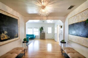 A spacious hallway with hardwood flooring, a modern chandelier, and large abstract paintings on the walls.