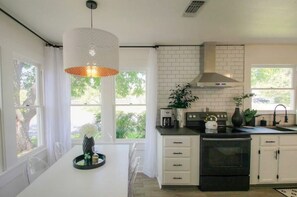 A modern kitchen with white cabinetry, a black stove, and a hanging pendant light.