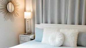 A bedroom with a bed, nightstand, lamp, and a decorative mirror. - Virginia Modern Luxe (Springfield)