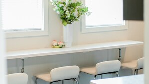 A room with a white desk, three white chairs, a white vase with flowers, and two windows with blinds. - Virginia Modern Luxe (Springfield)