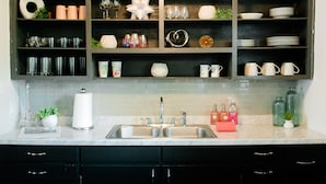 A kitchen with a marble countertop, a sink, and a shelf with various glassware and decorative items. - Virginia Modern Luxe (Springfield)