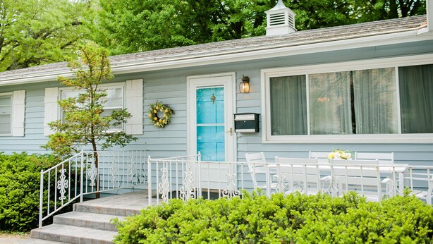 A light blue house with a front porch, a small tree, and a mailbox. - Peacock Palace (Springfield)
