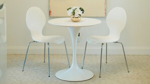 A dining area with a round table, two white chairs, a chandelier, and a large abstract painting on the wall. - Peacock Palace (Springfield)