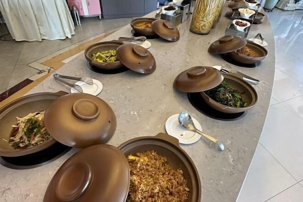 Un buffet composé de différents plats présentés dans de grands récipients ronds de couleur marron, certains étant dotés de couvercles, et des ustensiles de service disposés sur la table.