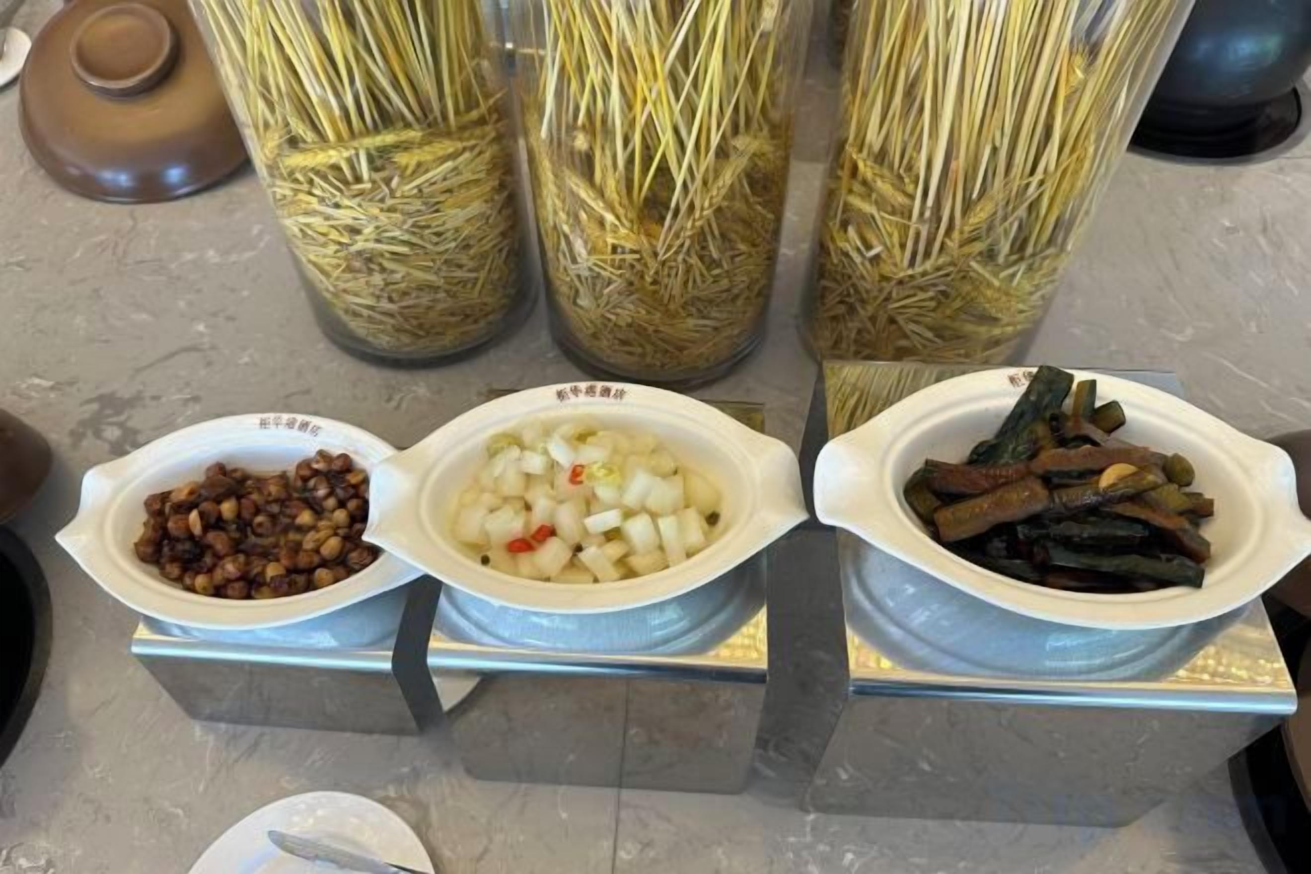 Tres platos de comida sobre una mesa, con contenedores de paja al fondo.