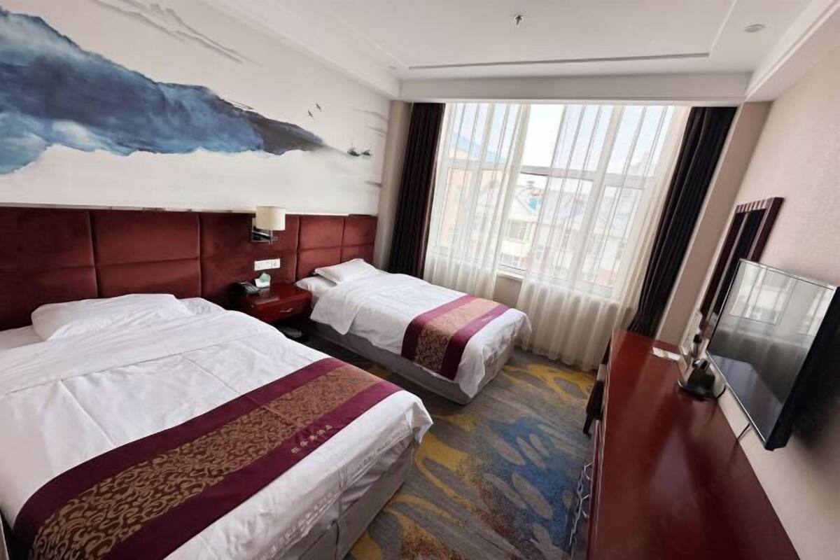 A hotel room with two beds, a large painting on the wall, a window with curtains, and a TV on the right side.