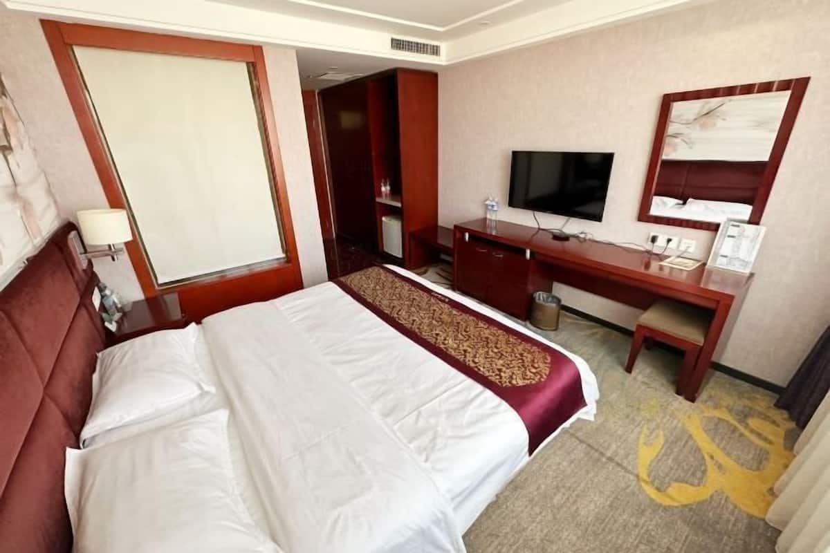 A hotel room with a bed, a desk, a television, and a mirror.