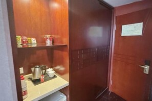 Une porte en bois, au-dessus de laquelle se trouve une petite étagère contenant une bouilloire, une tasse et quelques conserves.