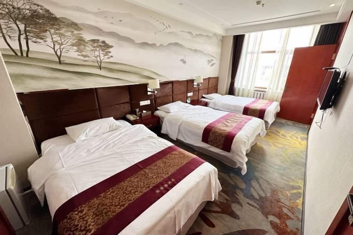 A hotel room with two beds, a mural on the wall, and a large window.