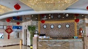 A hotel reception area with a marble counter, clocks on the wall, and red lanterns.