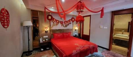 A bedroom with a red bedspread, a headboard, a bedside table, a lamp, and a wall decoration.