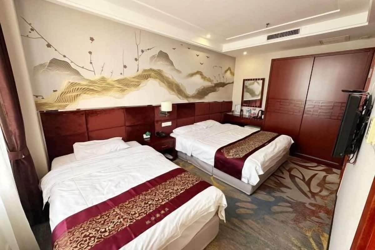 A hotel room with two beds, a large mural, a wardrobe, and a television.