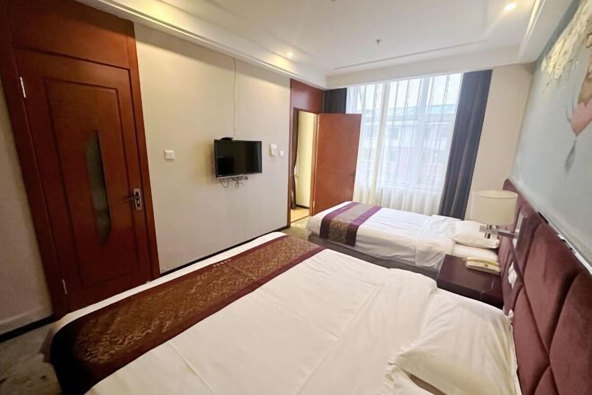 Une chambre d’hôtel avec deux lits, une télévision, une grande fenêtre avec des rideaux et une porte.