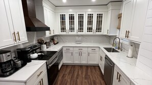A modern kitchen with white cabinetry, a central island, and a dark wood floor. - Wow! Only 3 min to Gore Mtn! King bed too (North Creek)