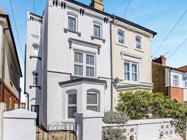 A two-story building with a white facade, multiple windows, and a small balcony. - 6 bedroom accommodation in Ramsgate (Ramsgate)