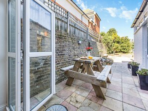 A patio with a wooden table and benches, a brick wall, and a clear sky. - 6 bedroom accommodation in Ramsgate (Ramsgate)