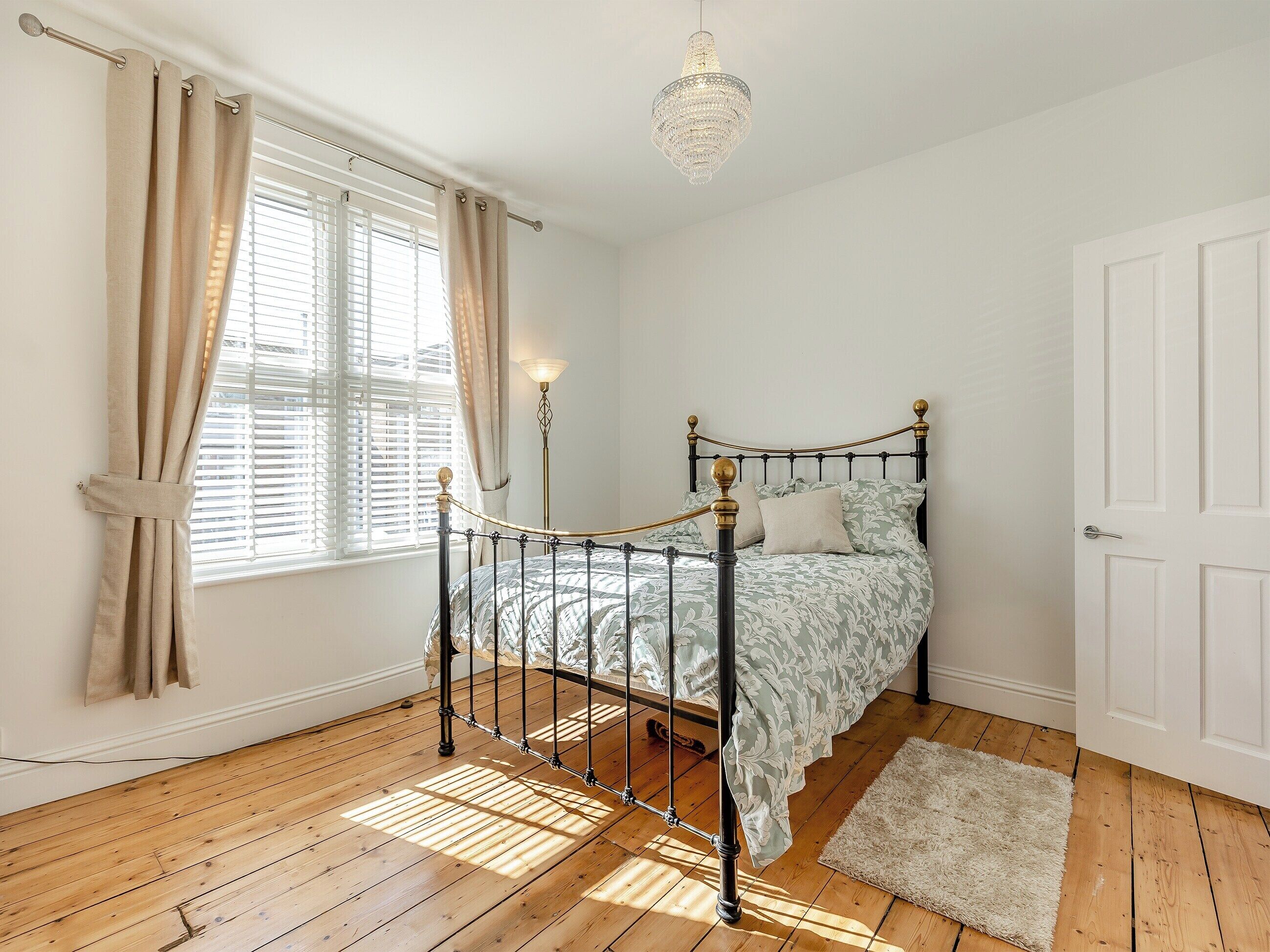 Een slaapkamer met een bed, gordijnen, een kroonluchter en een houten vloer.