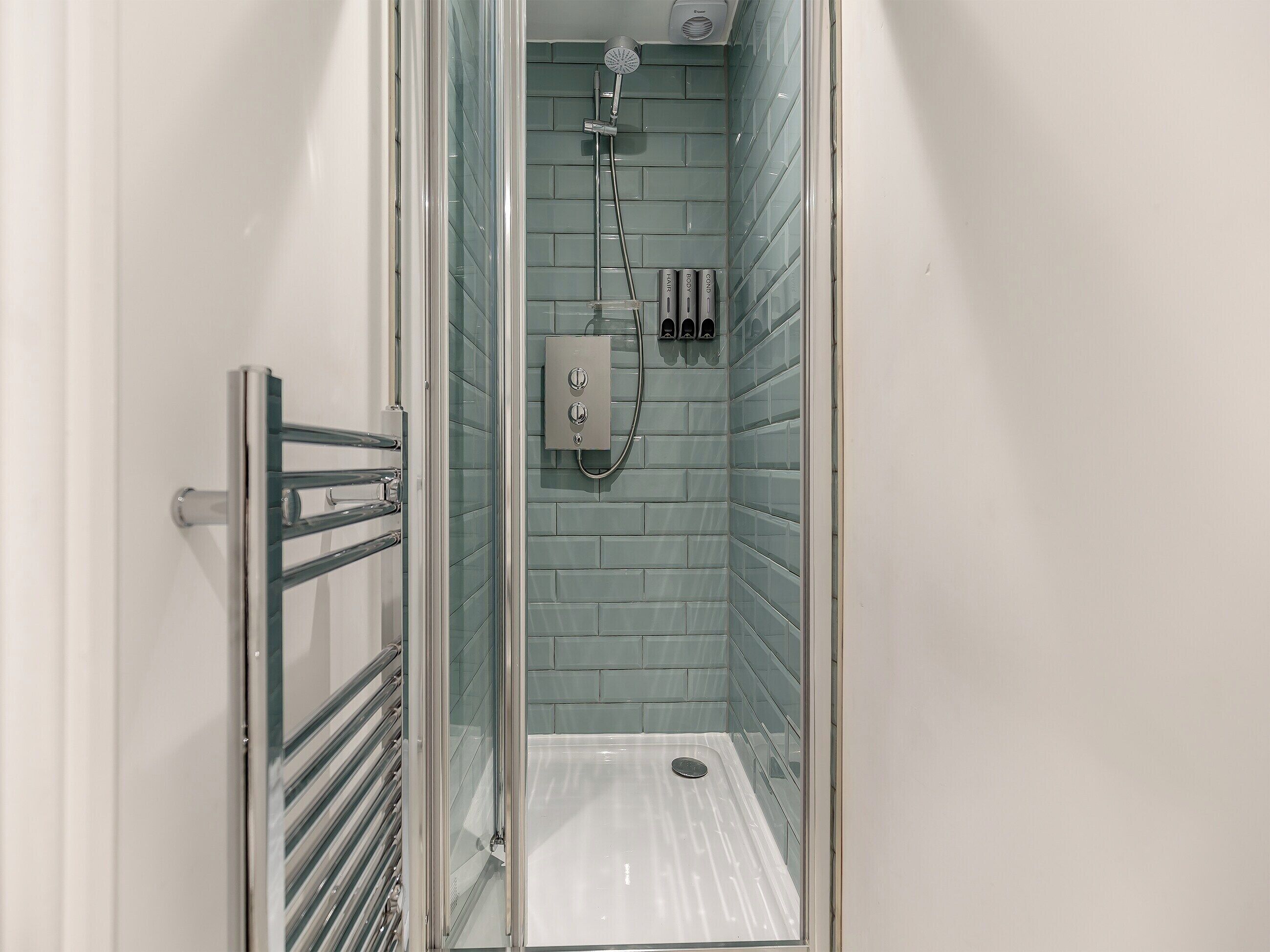 A glass-enclosed shower with a tiled wall, a control panel, and a metal handrail.