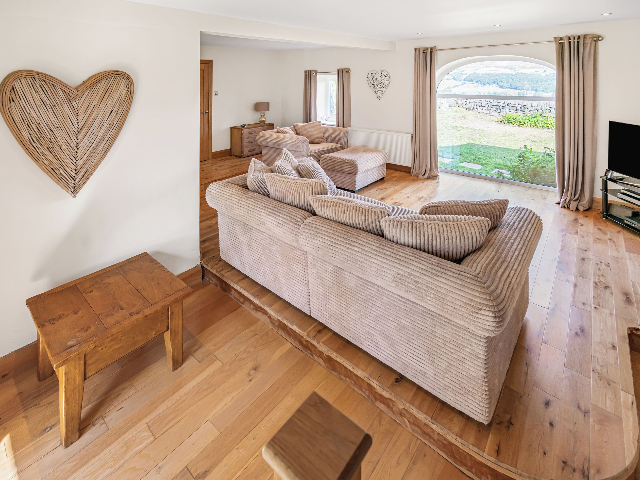 Ein großzügiger Wohnbereich mit einer großen Couch, einer Holzbank und Blick auf einen Garten durch ein großes Fenster.