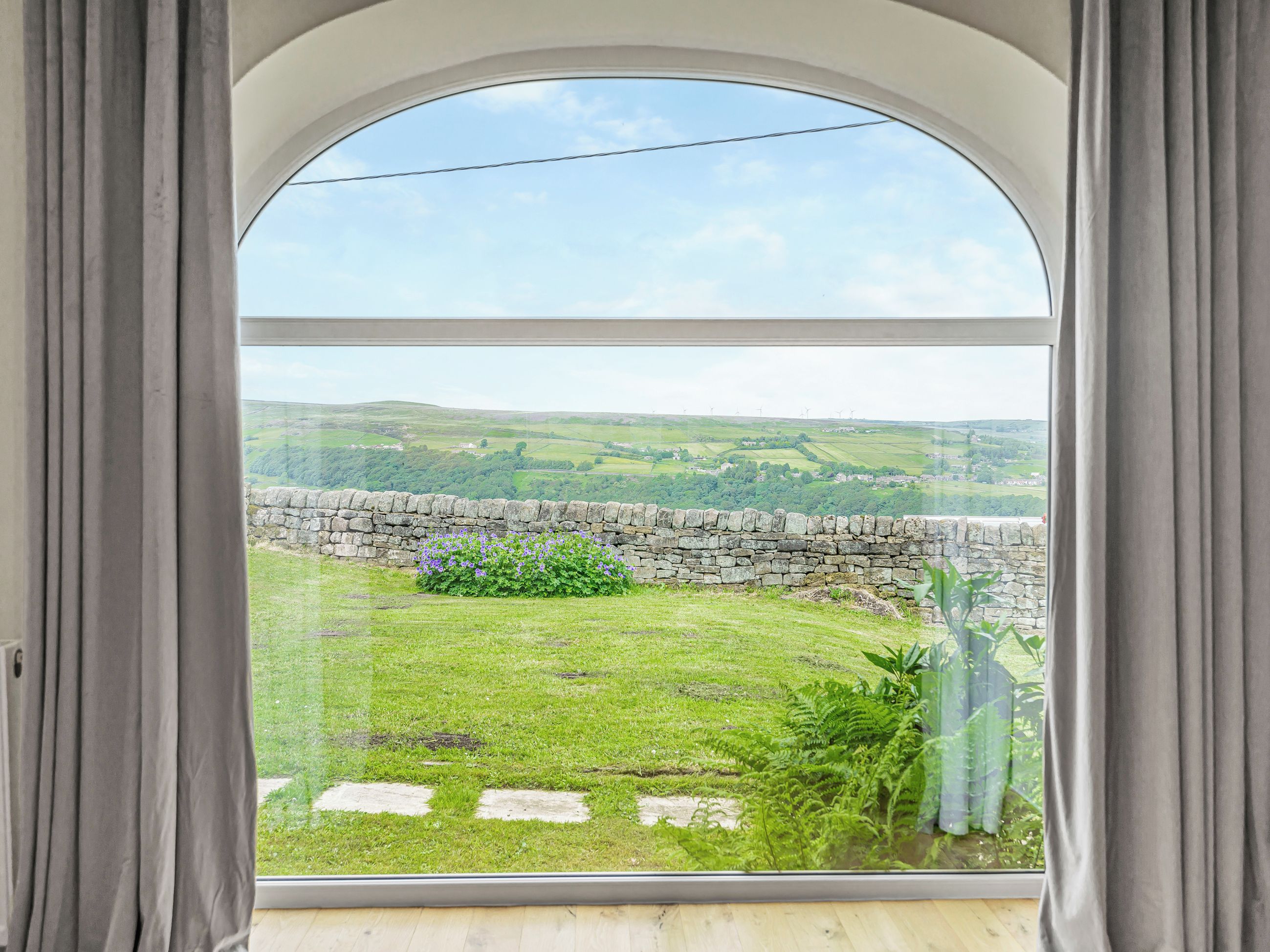 A room with a large arched window overlooking a grassy yard with a stone wall and a stone pathway.