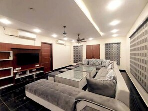 Un salon moderne doté d’un téléviseur à écran plat, d’un ensemble de canapés, d’une table basse en verre et d’un ventilateur de plafond.