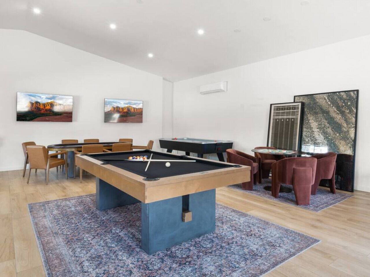 A pool table in a room with a dining area and two paintings on the wall.