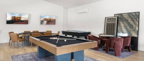 A pool table in a room with a dining area and two paintings on the wall.