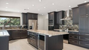 A modern kitchen with dark cabinetry, a large island, and a stone backsplash.