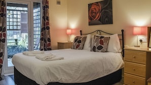 A bedroom with a bed, two bedside tables, a nightstand, a window with curtains, and a painting on the wall.