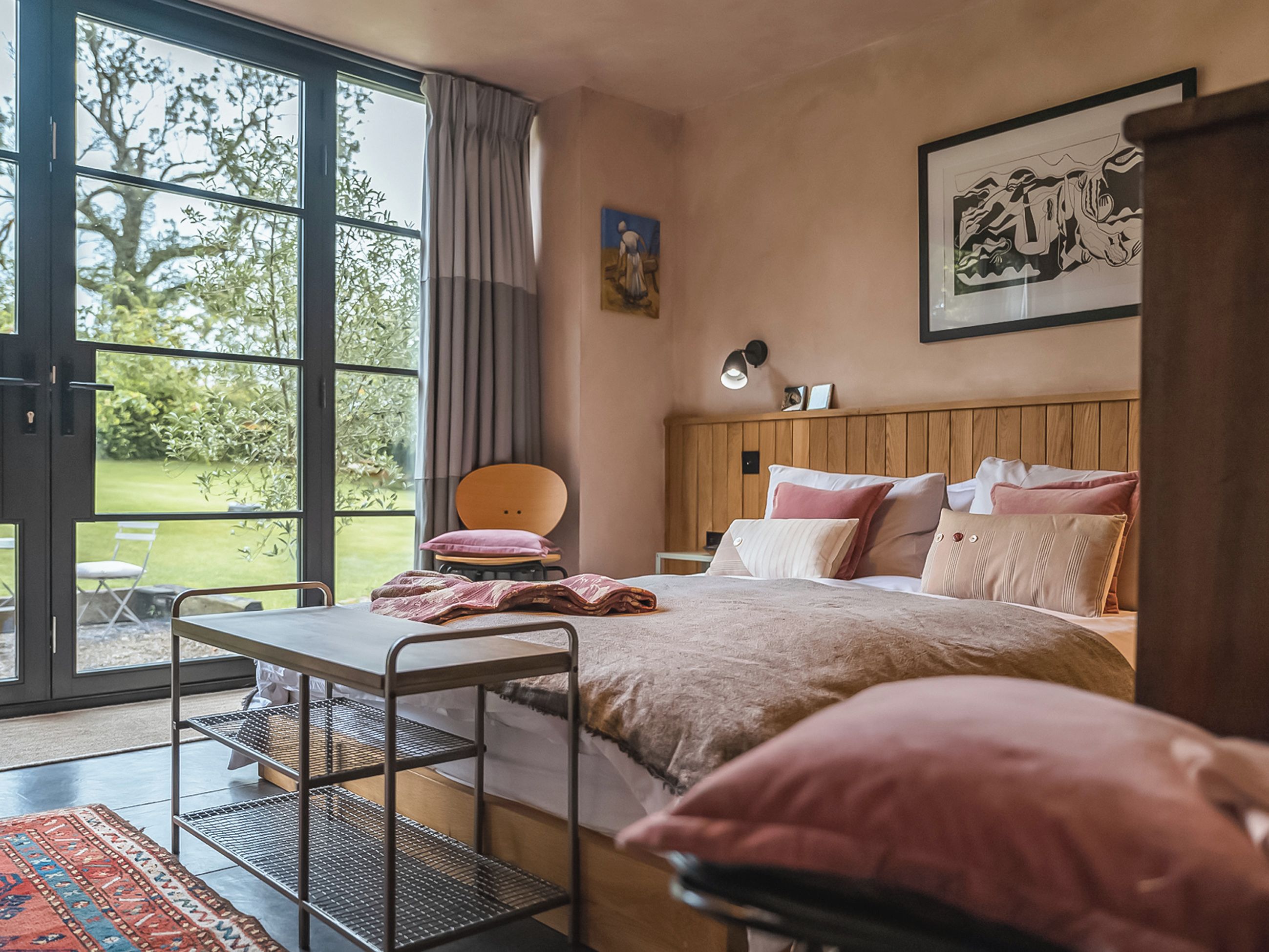 Ein Schlafzimmer mit Bett, Sessel, Tisch und Fenster mit Blick auf Grünflächen.