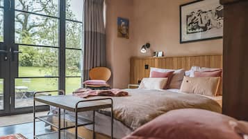 Ein Schlafzimmer mit Bett, Sessel, Tisch und Fenster mit Blick auf Grünflächen.