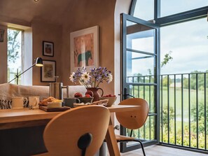 A modern dining area with a wooden table, chairs, and a vase of flowers. A large window offers a view of greenery outside. - 1 bedroom accommodation in Willington, near Tarporley (Willington, near Tarporley)