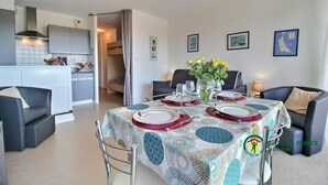 Ein Essbereich mit einem für vier Personen gedecktem Tisch, eine Küche im Hintergrund und ein Bett im angrenzenden Zimmer.