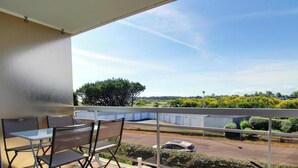 Ein Balkon mit Tisch und Stühlen, ein kleiner runder Tisch sowie Blick auf eine Straße und Grünflächen.
