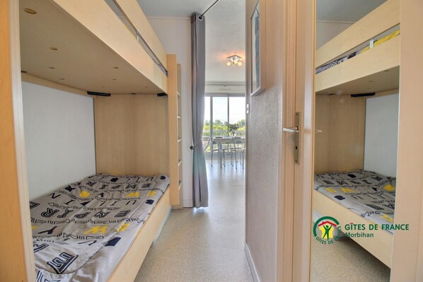 Un dormitorio con literas, un pasillo que da a un balcón y vistas al exterior.