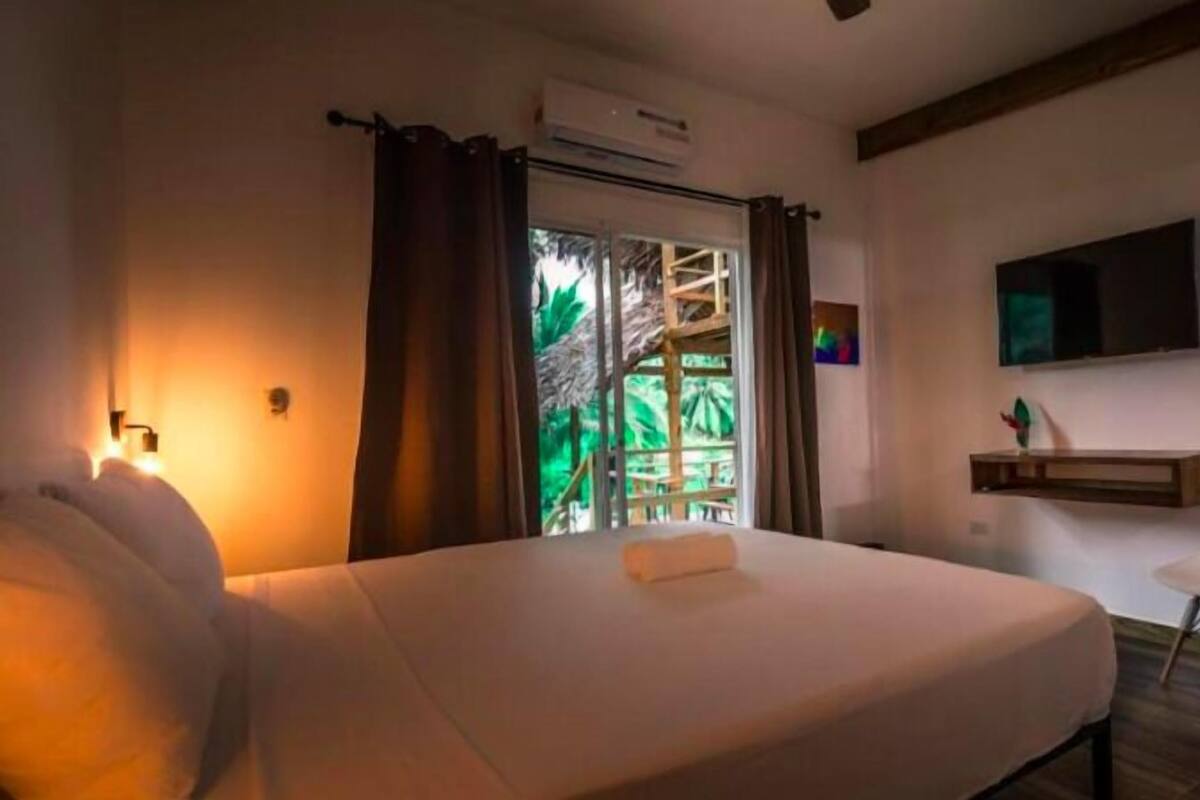 A hotel room with a bed, a desk, a chair, a TV, and a window with curtains.