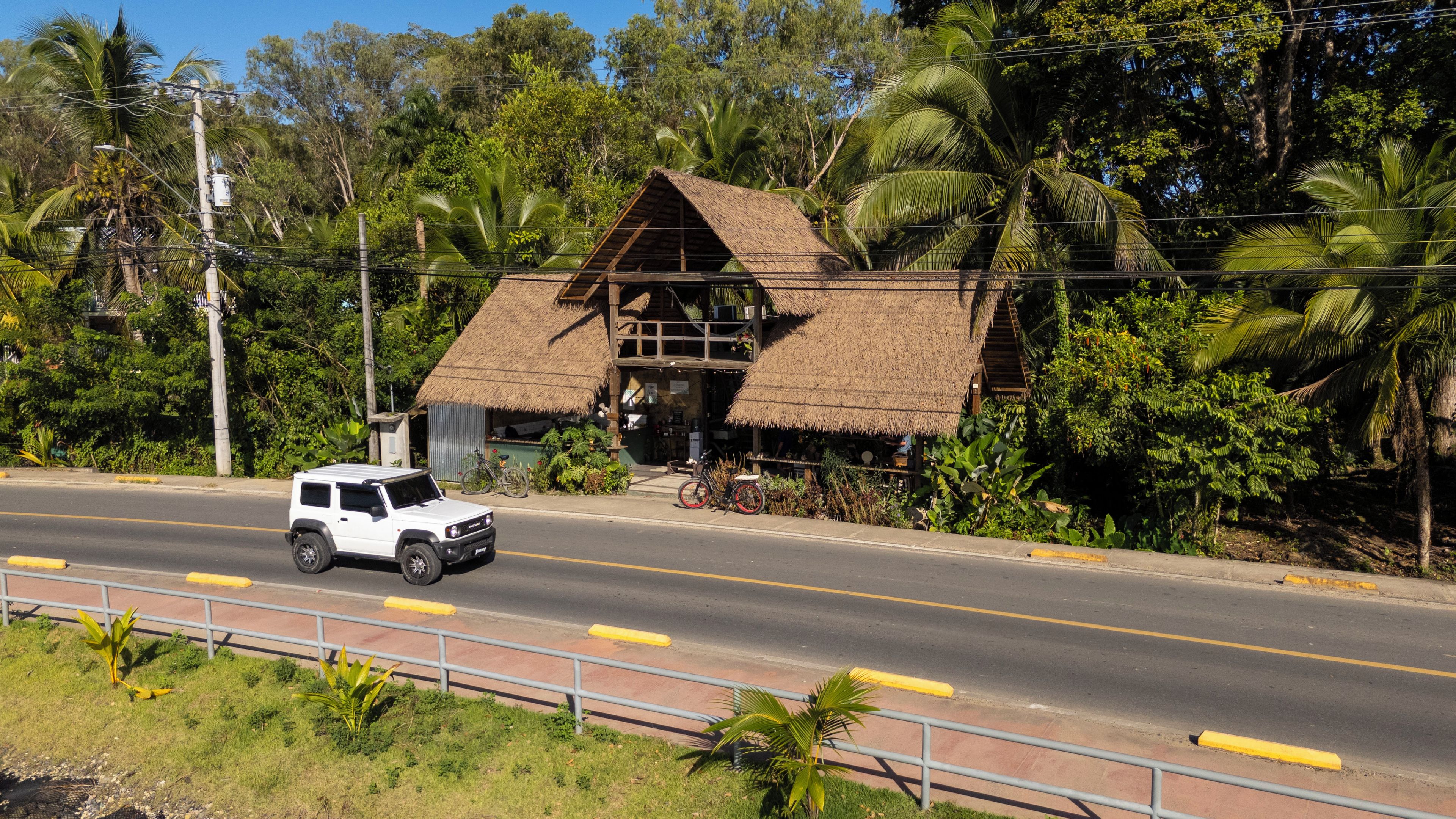 A white SUV parked in front of a thatched-roof building with a staircase leading to the entrance.