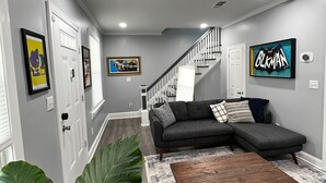 Ein modernes Wohnzimmer mit einem grauen Sofa, einem Holztisch und großen Grünpflanzen.