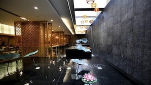 A modern hotel lobby with a reflective floor, a water feature with lotus flowers, and a traditional wooden partition. - Dongquan Hot Spring Holiday Hotel (Dalian)