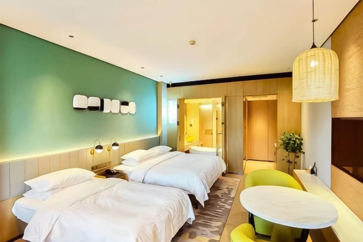Habitación de hotel con dos camas, un área de descanso con una mesa y una lámpara fijada a la pared.