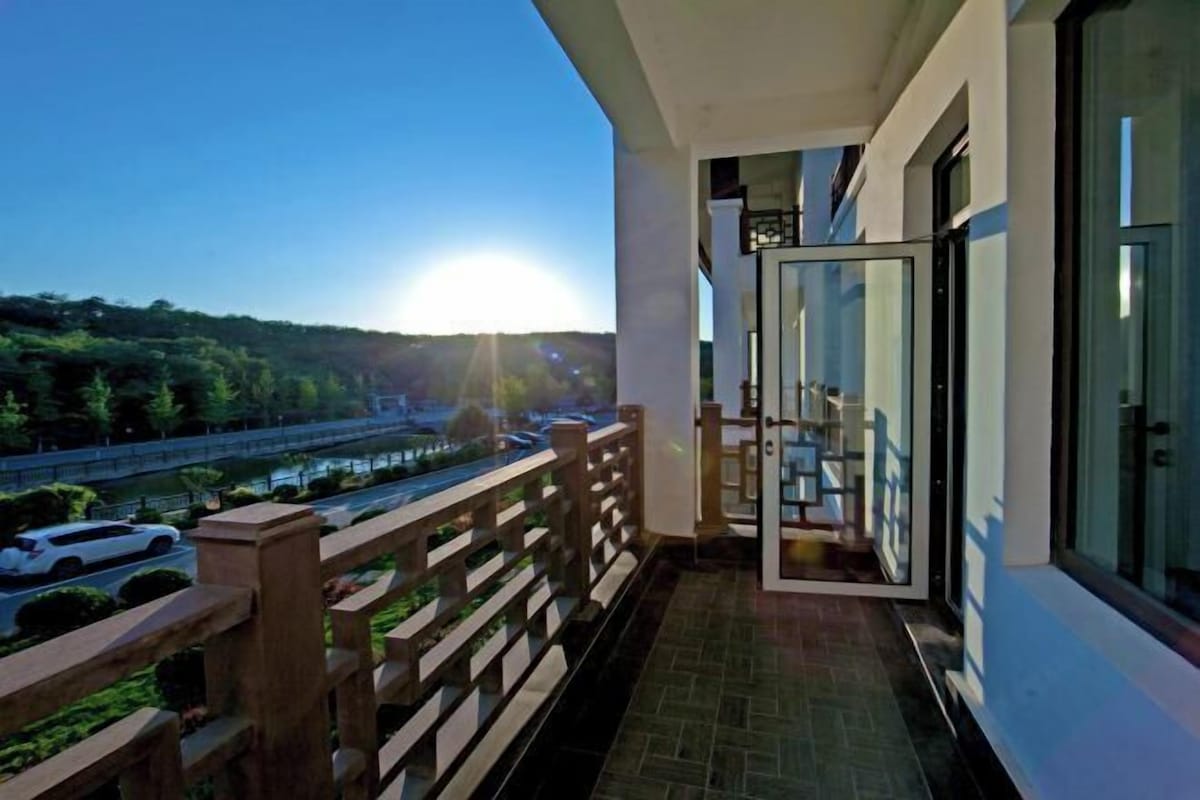 A balcony with a view of a road and greenery, a glass door, and a tiled floor.
