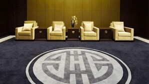 A lobby with five beige armchairs arranged in a row, a central table with a vase, and a large circular logo on the floor. - Dongquan Hot Spring Holiday Hotel (Dalian)