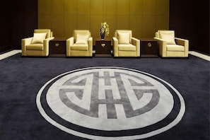 A lobby with five beige armchairs arranged in a row, a central table with a vase, and a large circular logo on the floor. - Dongquan Hot Spring Holiday Hotel (Dalian)