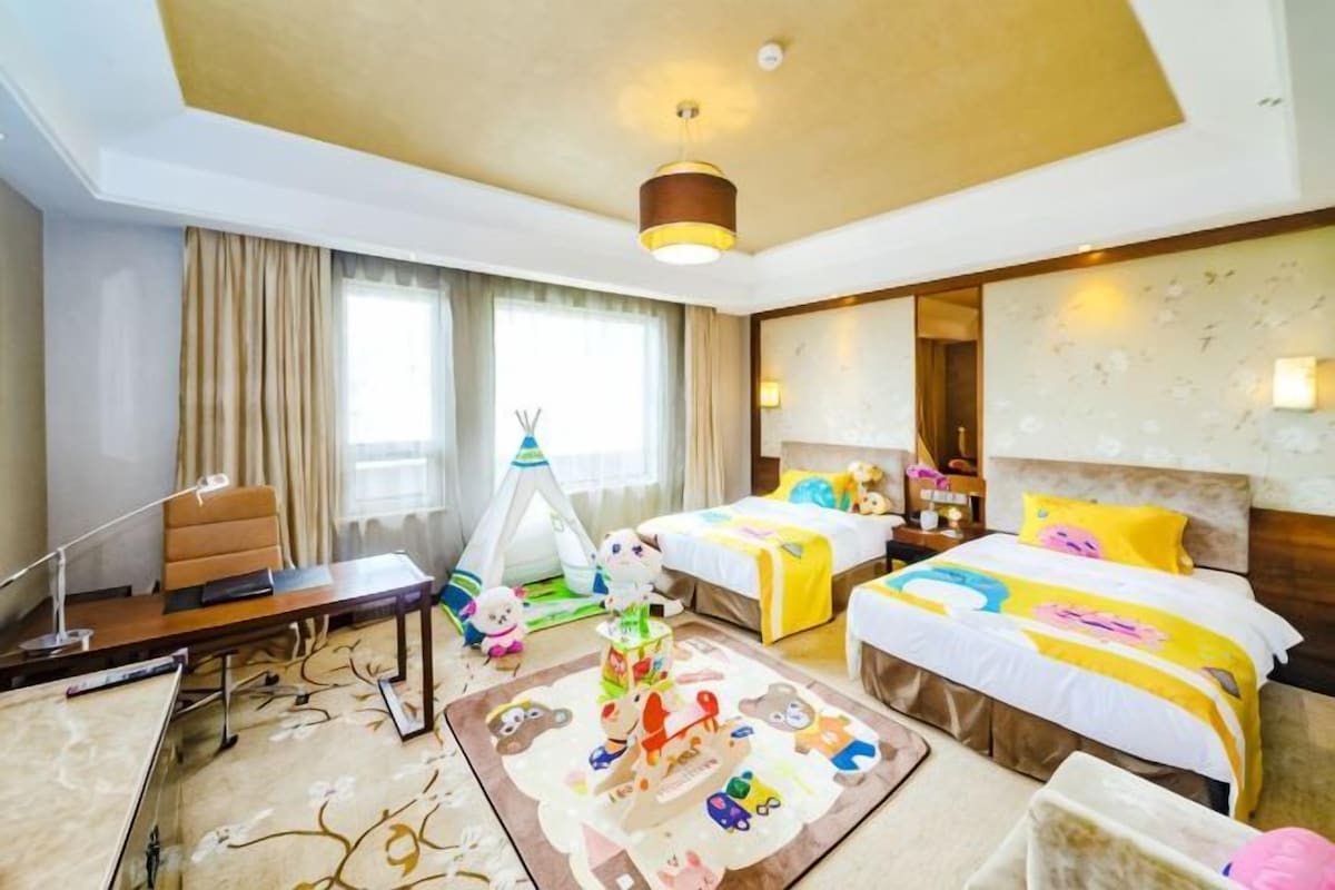 Habitación de hotel con dos camas, un escritorio, una silla, una lámpara de escritorio, una ventana con cortinas, una lámpara de pared y una alfombra decorativa.
