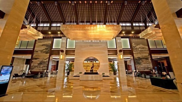 A spacious lobby with a high ceiling, a central fountain, and a reception desk. - Dongquan Hot Spring Holiday Hotel (Dalian)