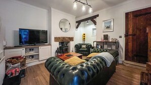 A cozy living room with a leather sofa, a television, a fireplace, and a wooden door. - 3 bedroom accommodation in Utley, near Haworth (Utley, near Haworth)