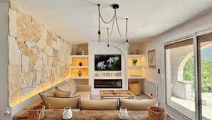 A cozy living room with a stone wall, a wooden dining table, a sofa, and a TV.