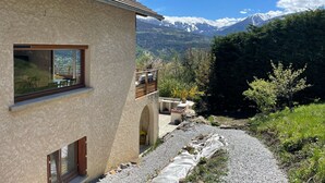 A house with a view of snow-capped mountains, a gravel path, and a wooden balcony.