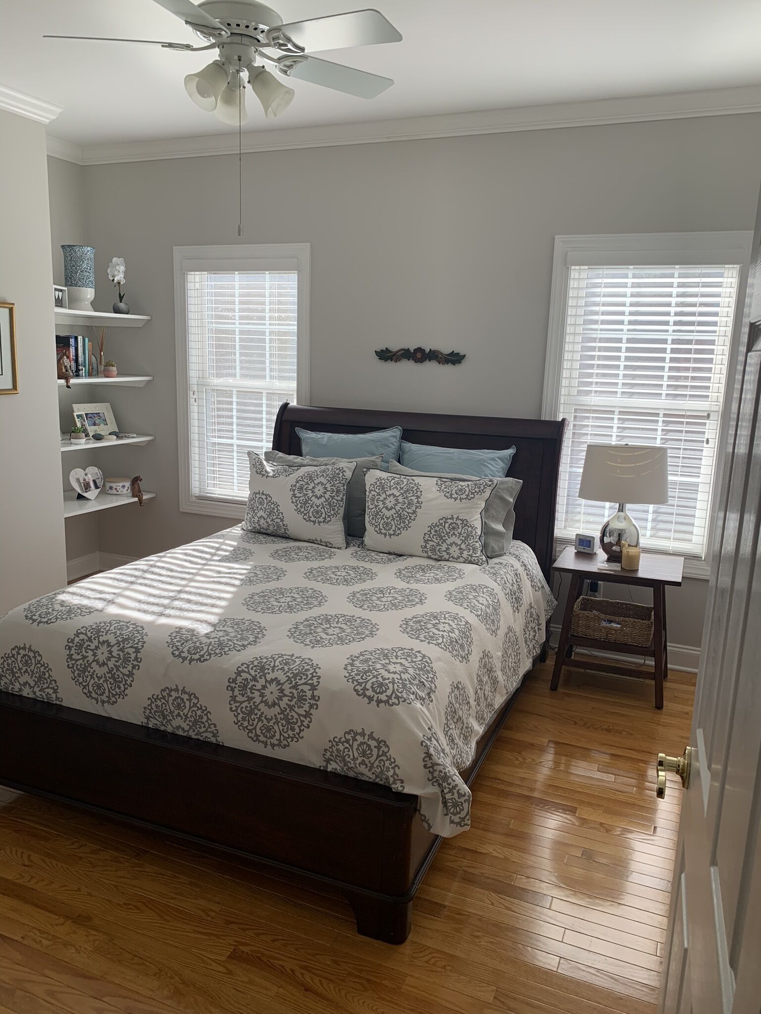 A bedroom with a bed, wooden floor, ceiling fan, and a window with blinds.