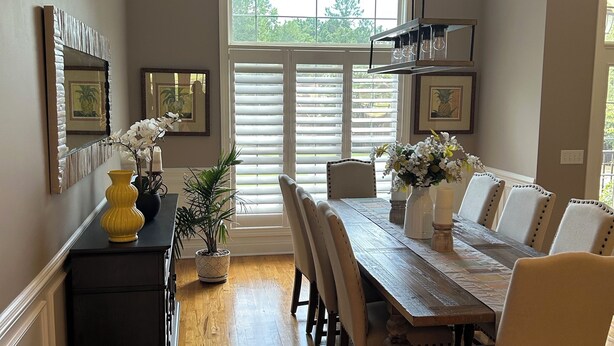 A dining area with a wooden table, white upholstered chairs, and a large window with blinds. - Master’s Rental - Golf course view in Woodside’s beautiful gated community! (Aiken)